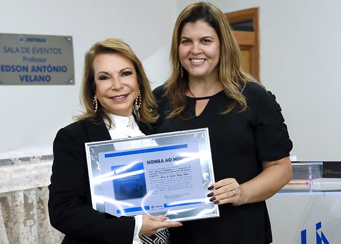 Profa. Maria do Rosário Araújo Velano, reitora da UNIFENAS, recebe o certificado das mãos da Profa. Sandra de Souza Alves, integrante da comissão organizadora do Sinais